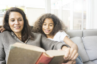 Mother and daughter sitting on couch reading a book - MOEF00323