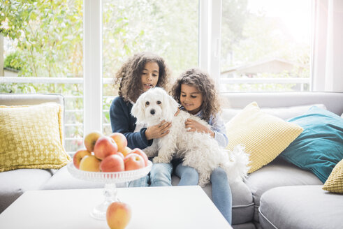 Schwestern sitzen auf der Couch und streicheln den kleinen weißen Hund - MOEF00327