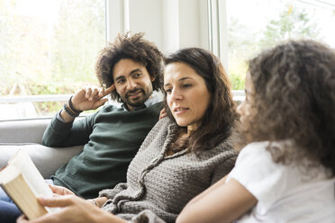 Glückliche Familie sitzt auf der Couch und liest ein Buch - MOEF00350