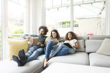 Glückliche Familie sitzt auf der Couch und liest Bücher - MOEF00352