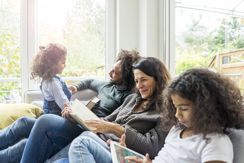 Glückliche Familie sitzt auf der Couch und liest Bücher - MOEF00355