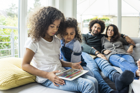 Glückliche Familie auf der Couch sitzend, Tochter spielt mit digitalem Tablet, lizenzfreies Stockfoto