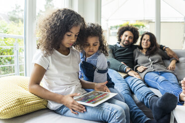 Glückliche Familie auf der Couch sitzend, Tochter spielt mit digitalem Tablet - MOEF00361