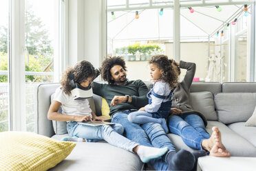 Glückliche Familie auf der Couch sitzend, Tochter spielt mit digitalem Tablet - MOEF00362