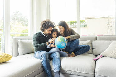 Happy family sitting on couch with globe, daughter learning geography - MOEF00363