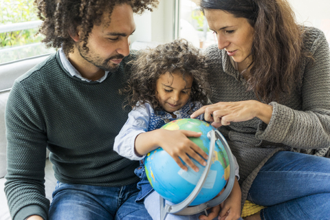 Glückliche Familie auf der Couch mit Globus, Tochter lernt Geografie, lizenzfreies Stockfoto