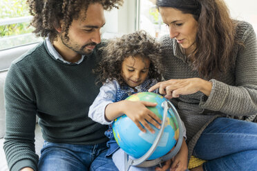 Happy family sitting on couch with globe, daughter learning geography - MOEF00364