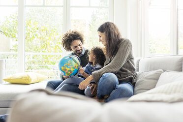 Happy family sitting on couch with globe, daughter learning geography - MOEF00365