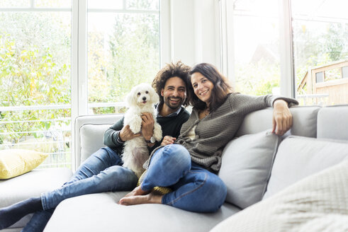 Glückliche Familie mit Hund sitzt zusammen im gemütlichen Wohnzimmer - MOEF00368