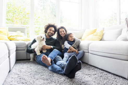 Glückliche Familie mit Hund sitzt zusammen im gemütlichen Wohnzimmer - MOEF00369