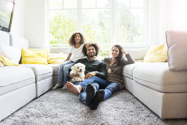 Glückliche Familie mit Hund sitzt zusammen im gemütlichen Wohnzimmer - MOEF00371