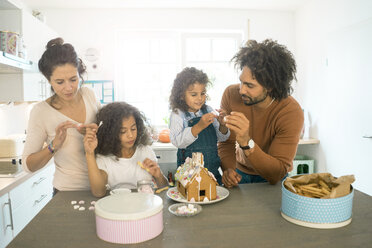 Familie klebt Lebkuchenhaus in Küche für Weihnachten mit Süßigkeiten - MOEF00378