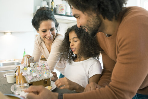 Familie klebt Lebkuchenhaus in Küche für Weihnachten mit Süßigkeiten - MOEF00383