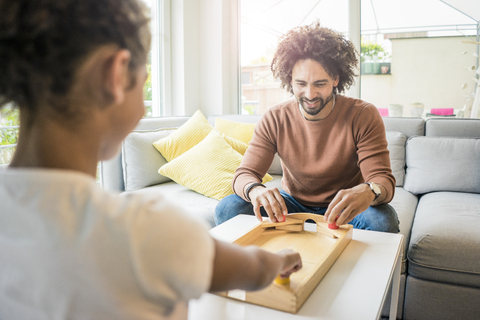 Vater und Tochter sitzen auf der Couch und spielen Tischfußball, lizenzfreies Stockfoto