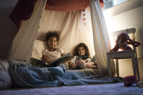 Zwei Schwestern sitzen in einem dunklen Kinderzimmer und lesen ein Buch - MOEF00403