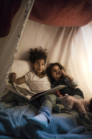 Zwei Schwestern sitzen in einem dunklen Kinderzimmer und lesen ein Buch, lizenzfreies Stockfoto