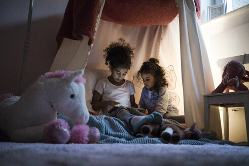 Two sisters sitting in dark children's room, looking at digital tablet - MOEF00409