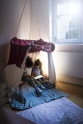Zwei Schwestern sitzen in einem dunklen Kinderzimmer und schauen auf ein digitales Tablet - MOEF00411