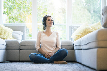 Frau sitzt allein auf der Couch und hört Musik mit Kopfhörern - MOEF00417