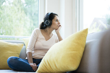 Woman sitting alone on couch, listening music with headphones - MOEF00418