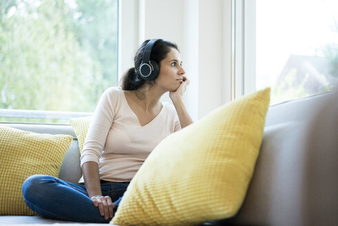 Frau sitzt allein auf der Couch und hört Musik mit Kopfhörern - MOEF00418