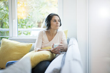 Frau sitzt allein auf der Couch und hört Musik mit Kopfhörern - MOEF00419