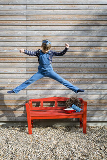 Girl jumping in the air in front of a wooden facade - OJF00208