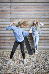 Two girls with skateboard in front of wooden facade - OJF00212
