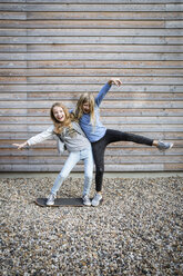 Zwei lachende Mädchen haben Spaß vor einer Holzfassade - OJF00213