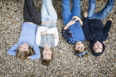 Drei Mädchen und ein Junge liegen auf dem mit Kieselsteinen bedeckten Boden - OJF00220