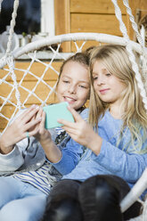 Porträt von zwei Mädchen, die sich in einem Hängesessel entspannen und ein Selfie mit ihrem Smartphone machen - OJF00221