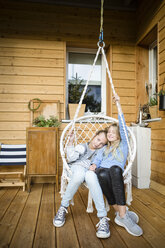 Zwei Mädchen entspannen sich in einem Hängesessel auf der Veranda - OJF00222