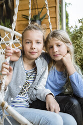 Portrait of two best friends sitting in a hanging chair on veranda - OJF00224