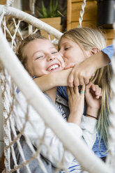 Girl hugging and kissing her best friend in a hanging chair - OJF00225