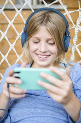 Porträt eines glücklichen Mädchens mit Kopfhörern und Smartphone in einem Hängesessel - OJF00226