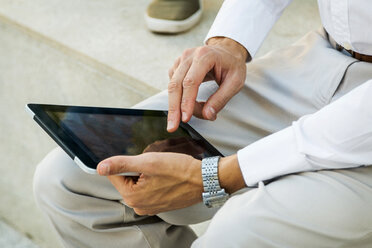 Geschäftsmann sitzt an der Wand und benutzt ein Tablet, Teilansicht - VABF01367