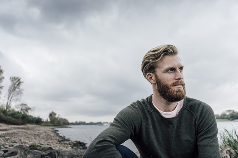 Junger Mann sitzend am Fluss im Herbst, Porträt, lizenzfreies Stockfoto