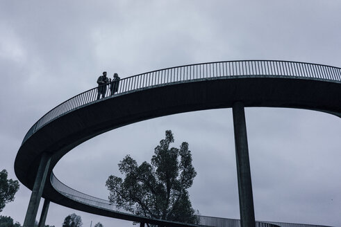 Zwei Geschäftsleute stehen auf einer dunklen Brücke und haben eine Besprechung - KNSF02917