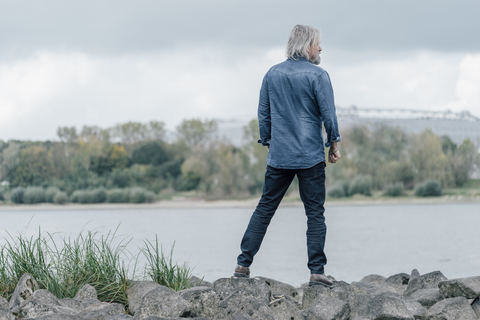 Älterer Mann steht auf Steinen und schaut auf den Rhein, lizenzfreies Stockfoto