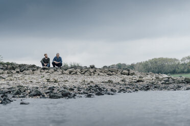 Father and son sitting at the river, talking together - KNSF02958