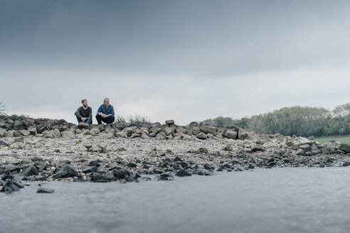 Vater und Sohn sitzen am Fluss und reden miteinander - KNSF02958