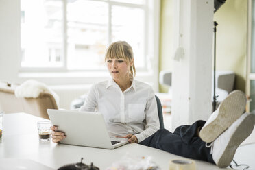 Businesswoman using laptop in office with feet on desk - JOSF01943