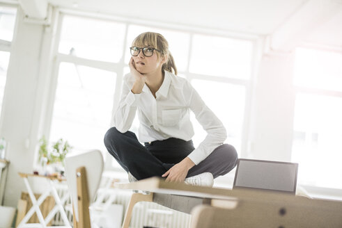 Businesswoman sitting on desk in office thinking - JOSF01947