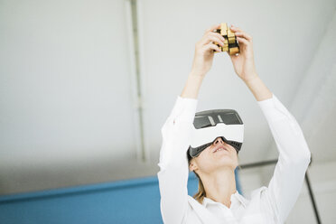 Businesswoman wearing VR glasses holding cubical structure - JOSF01976