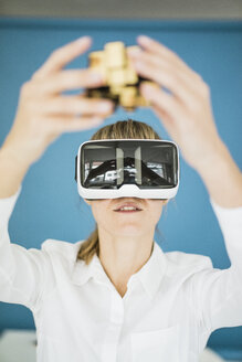 Businesswoman wearing VR glasses holding cubical structure - JOSF01978