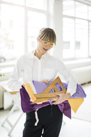 Lächelnde Modedesignerin mit Textilien in der Hand, lizenzfreies Stockfoto