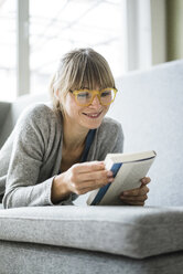 Smiling woman lying on couch reading book - JOSF01993