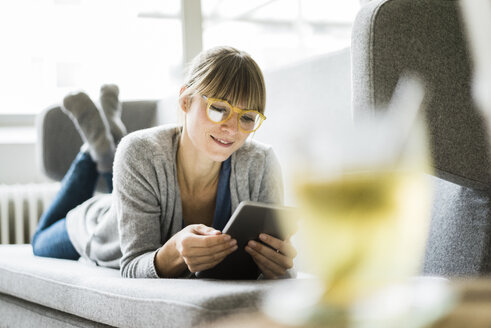 Lächelnde Frau auf der Couch liegend mit Tablet - JOSF01995