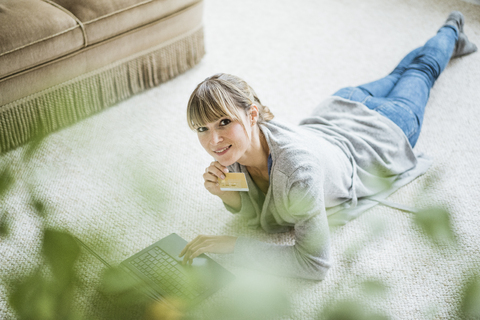 Lächelnde Frau auf dem Boden liegend mit Kreditkarte und Laptop, lizenzfreies Stockfoto