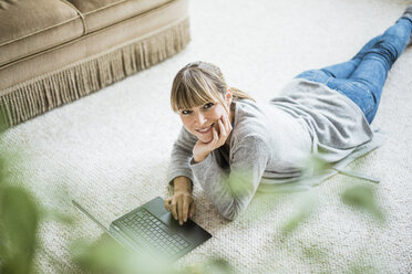 Smiling woman lying on the floor using laptop - JOSF01998